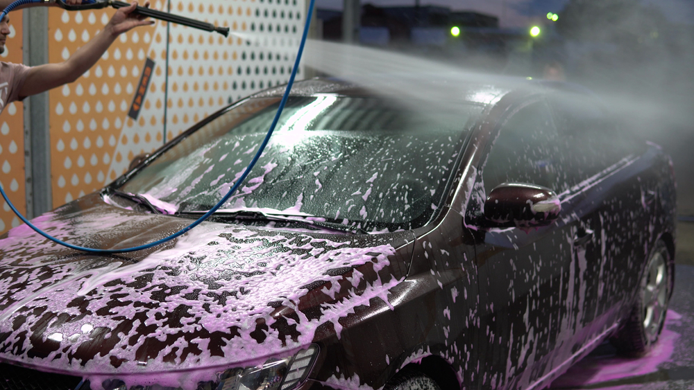 A man sprays down a soapy black car as part of a car wash business.