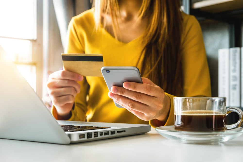 Woman holding a credit card and mobile phone while making an online purchase.